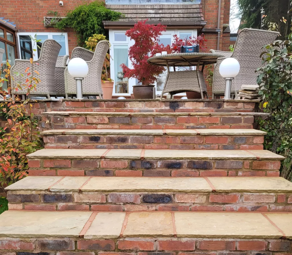 A step of stone built stairs leading to a patio with garden furniture