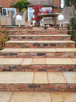 A yellow stone staircase leading up to a patio with garden furniture